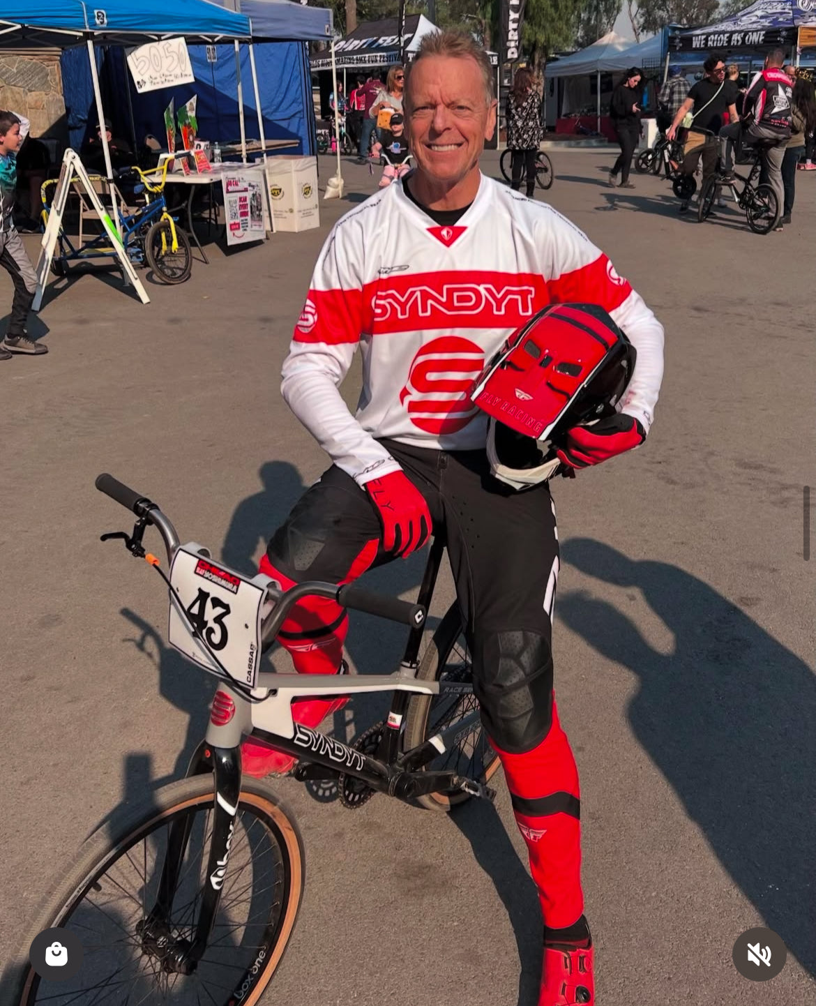 BMX Hall of Fame Stu Thomsen on his SYNDYT bike wearing  his SYNDYT white sports jersey with red large stripe around chest back and arms with a big SYNDYT "S"Logo under it.